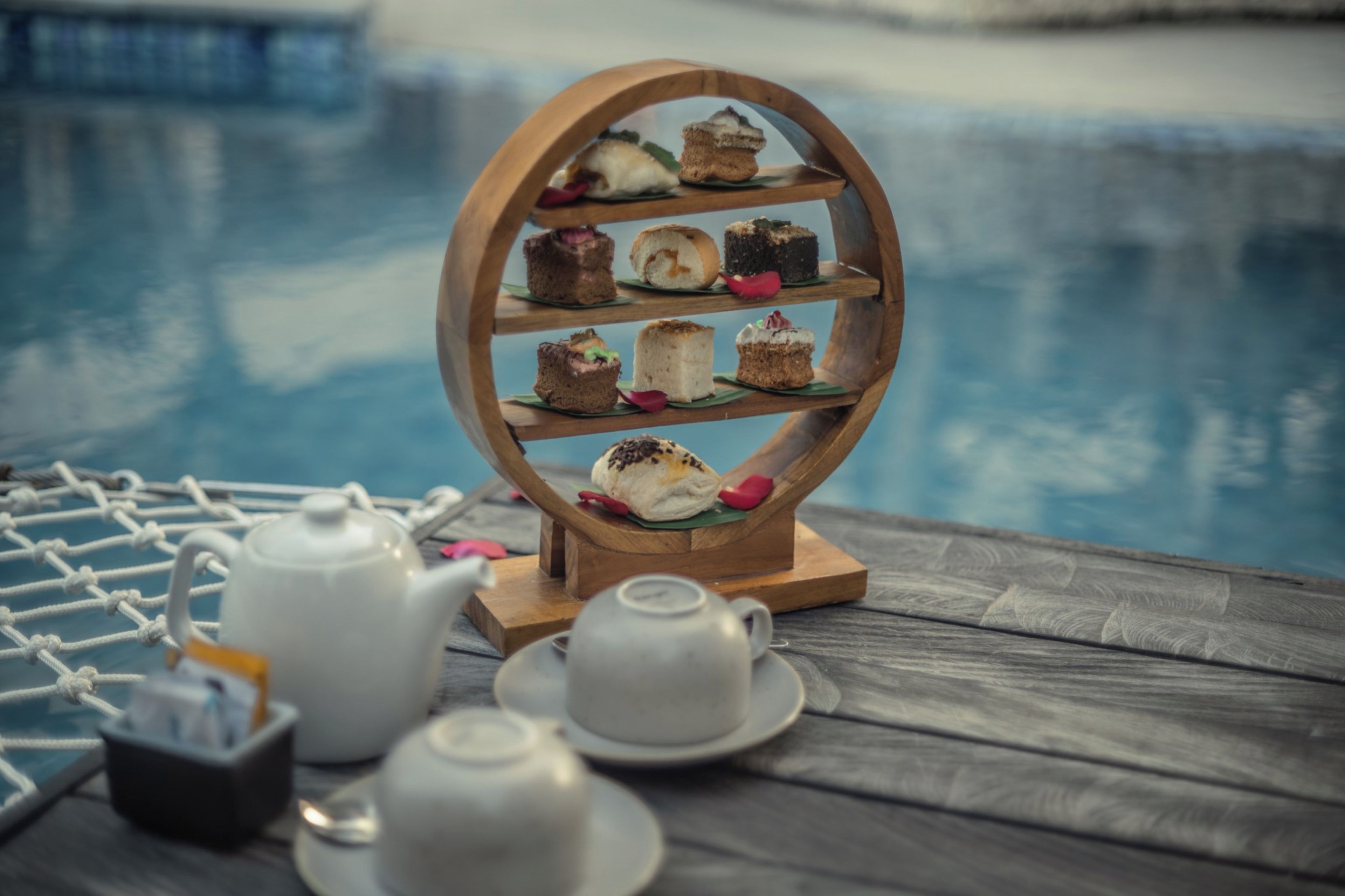 A wooden dessert stand with various pastries on a wooden table near a pool.