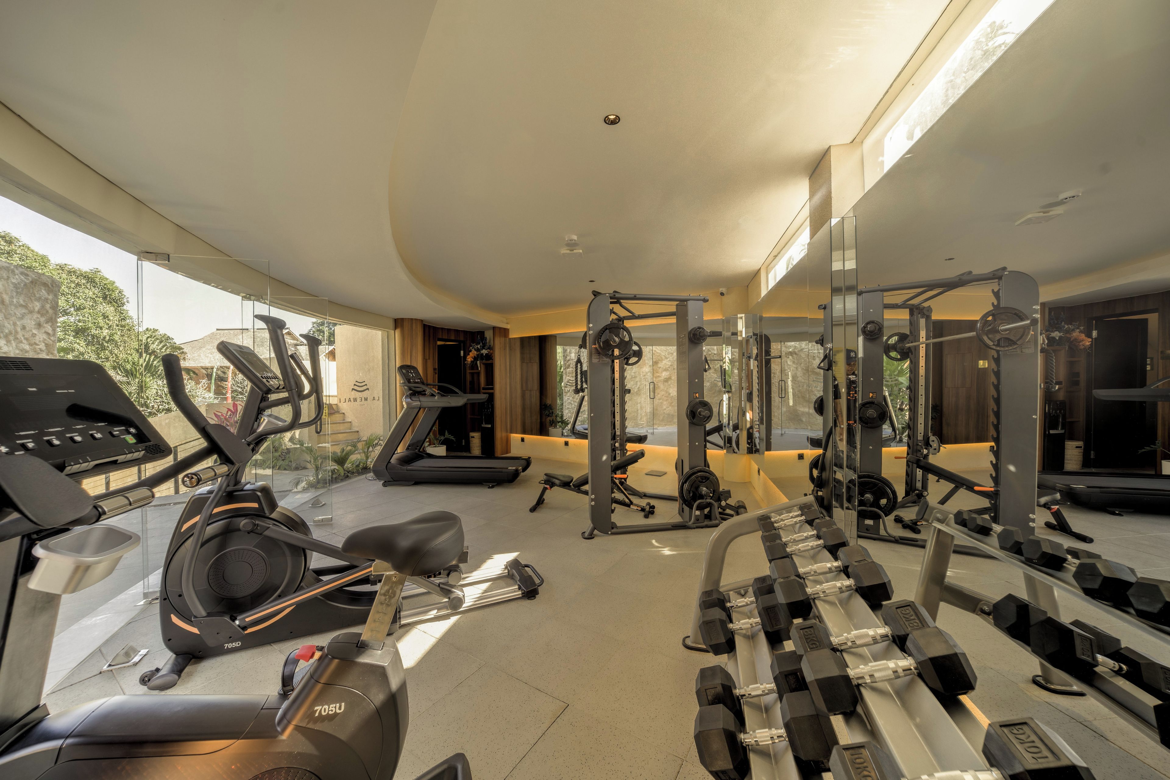 A gym with cardio machines, free weights, and mirrors.