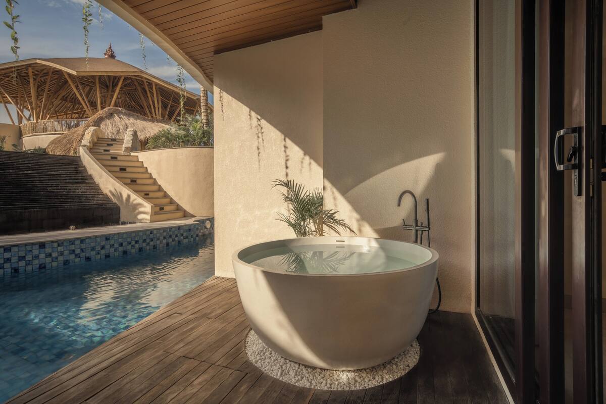 A modern bathroom with a freestanding bathtub, a wooden deck, and a pool.
