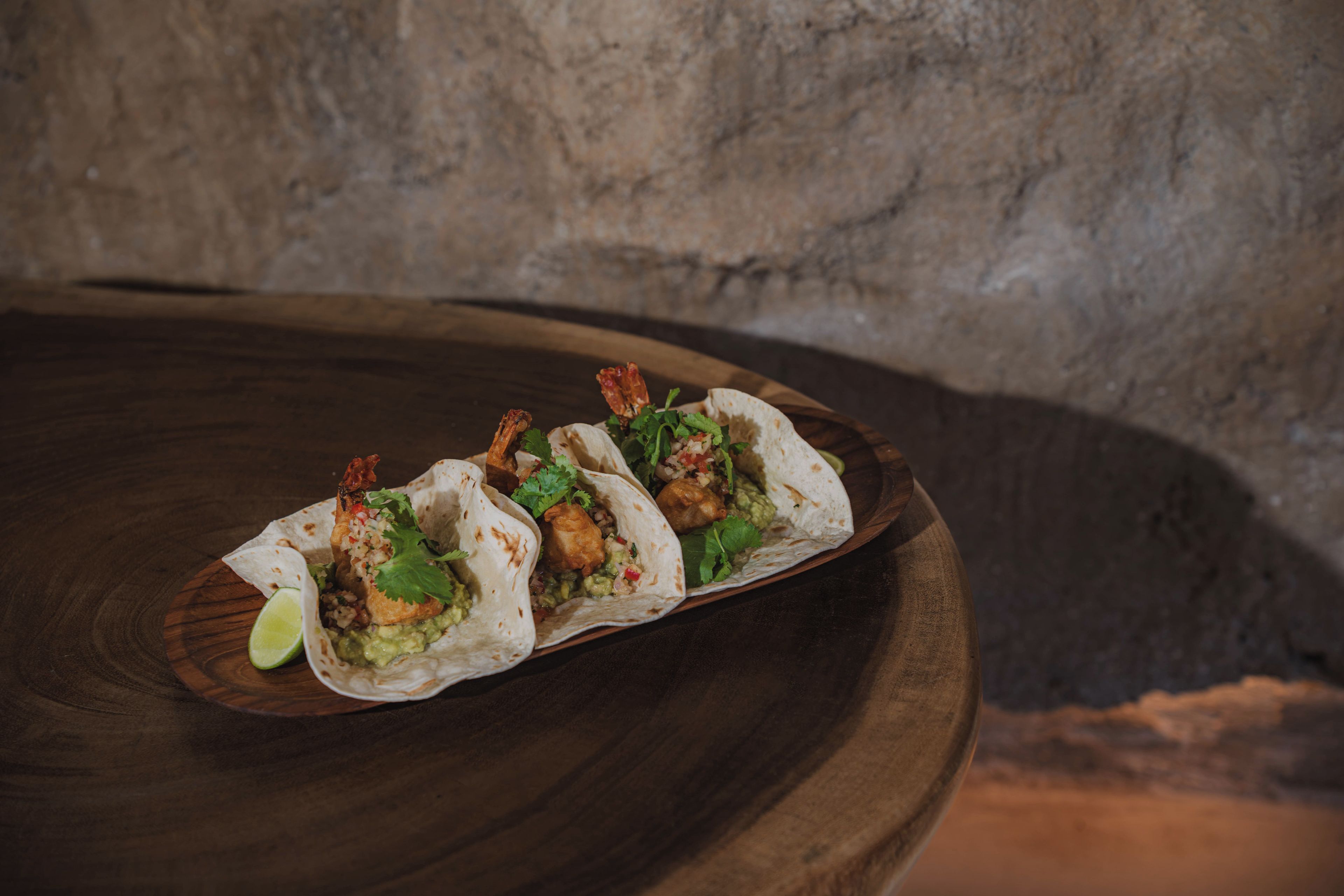 Three tacos on a wooden board with a lime wedge.