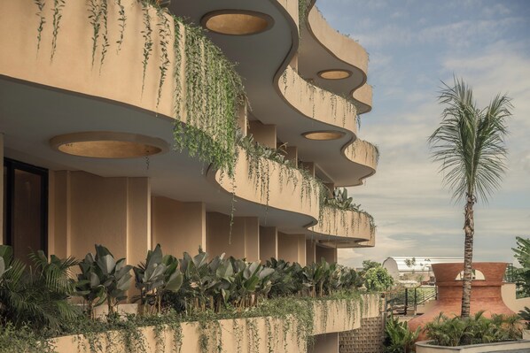 Un edificio moderno con balcones curvos, plantas colgantes y una palmera.