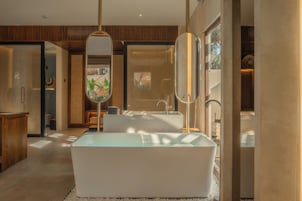 Ein modernes Badezimmer mit einer freistehenden Badewanne, einem großen Spiegel und einem Holzkosmetikschrank.