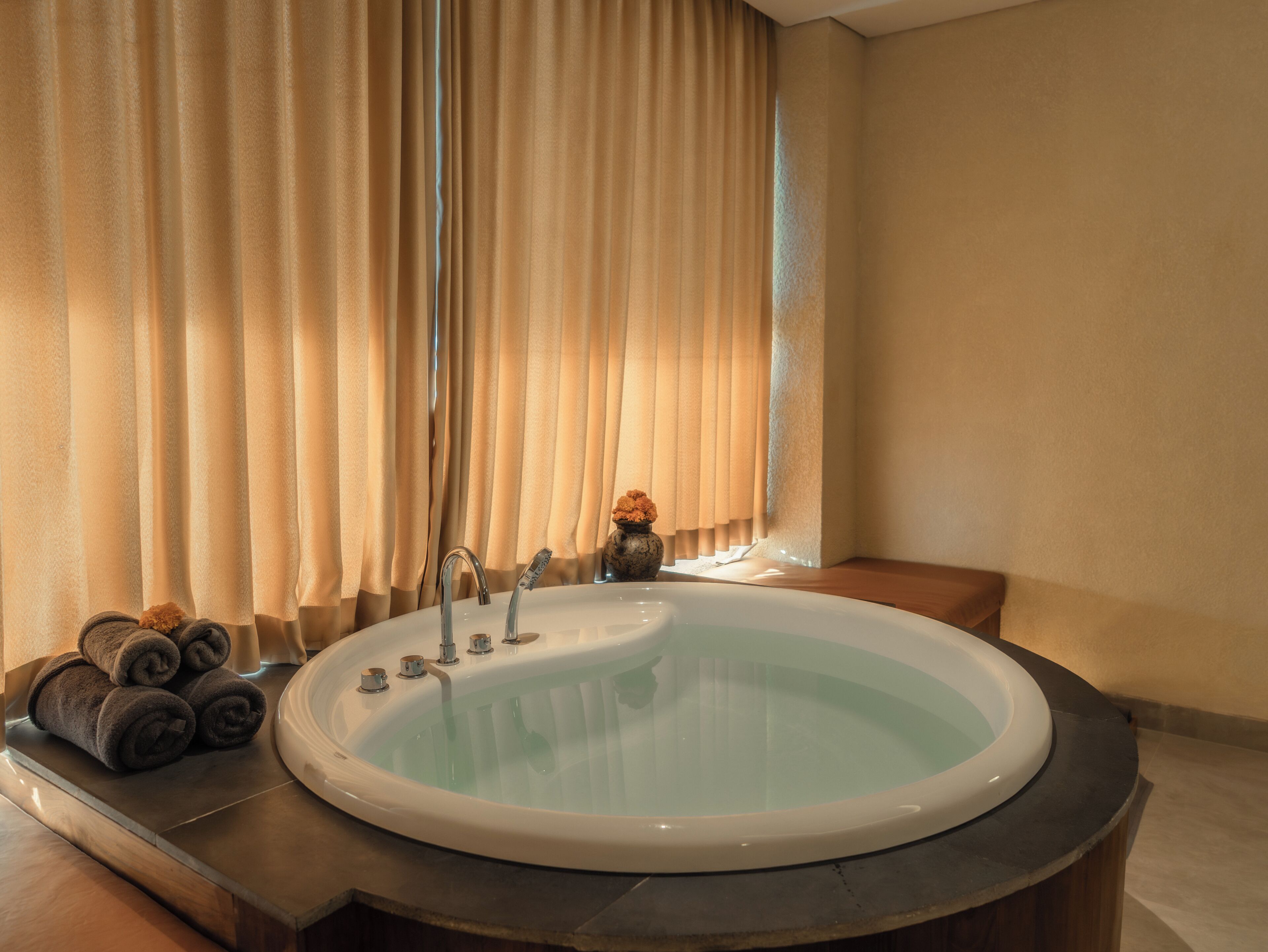 A bathroom with a bathtub, a towel rack with towels, and a window with curtains.