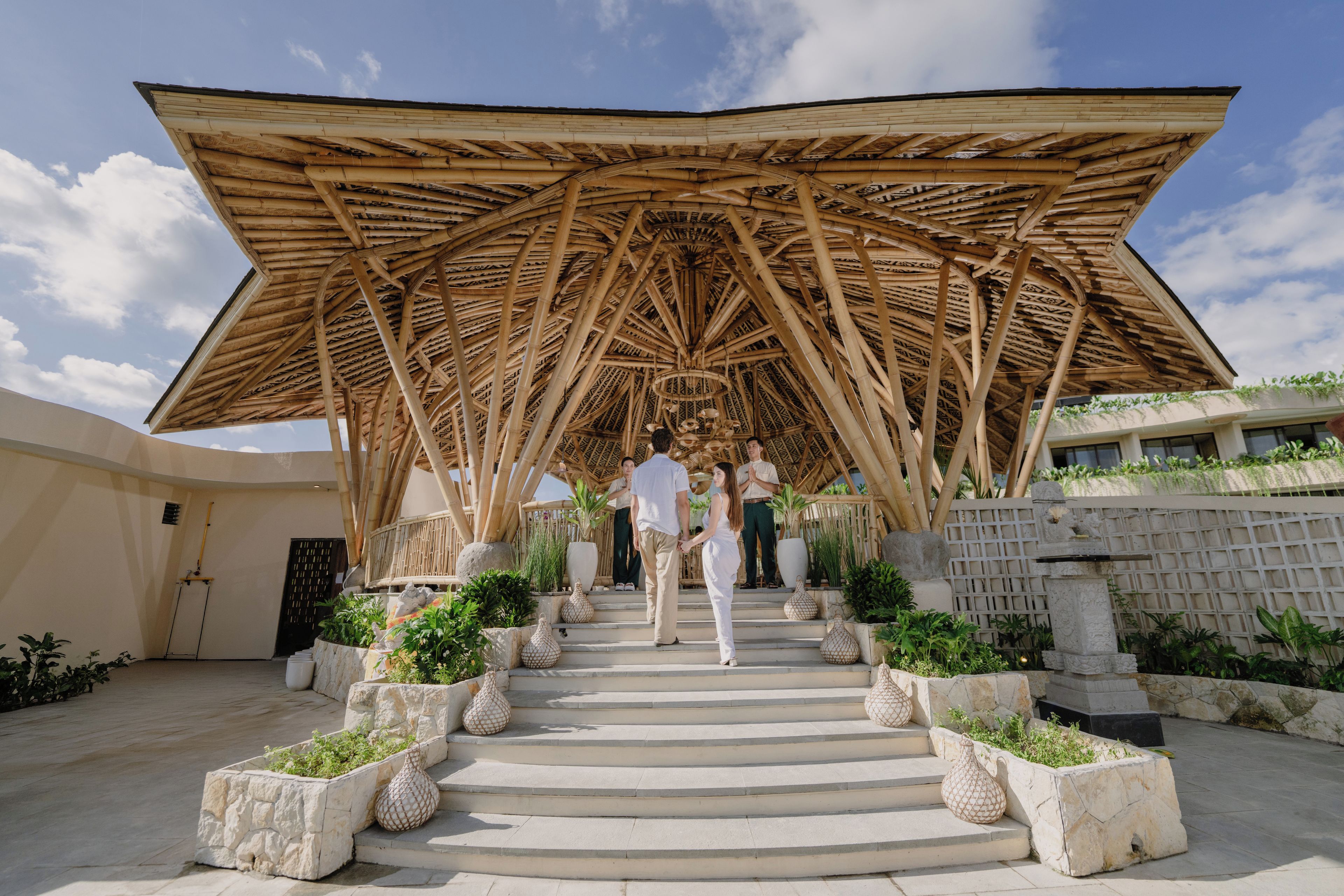 A modern architectural structure with a unique bamboo roof, a central staircase, and surrounding planters.