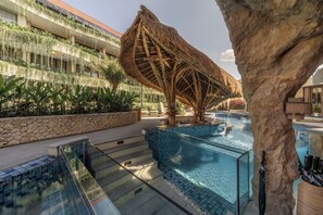 A resort pool area with a thatched-roof structure, a stone wall, and a glass balustrade. - La Mewali Resort Canggu by Ini Vie Hospitality (Canggu)