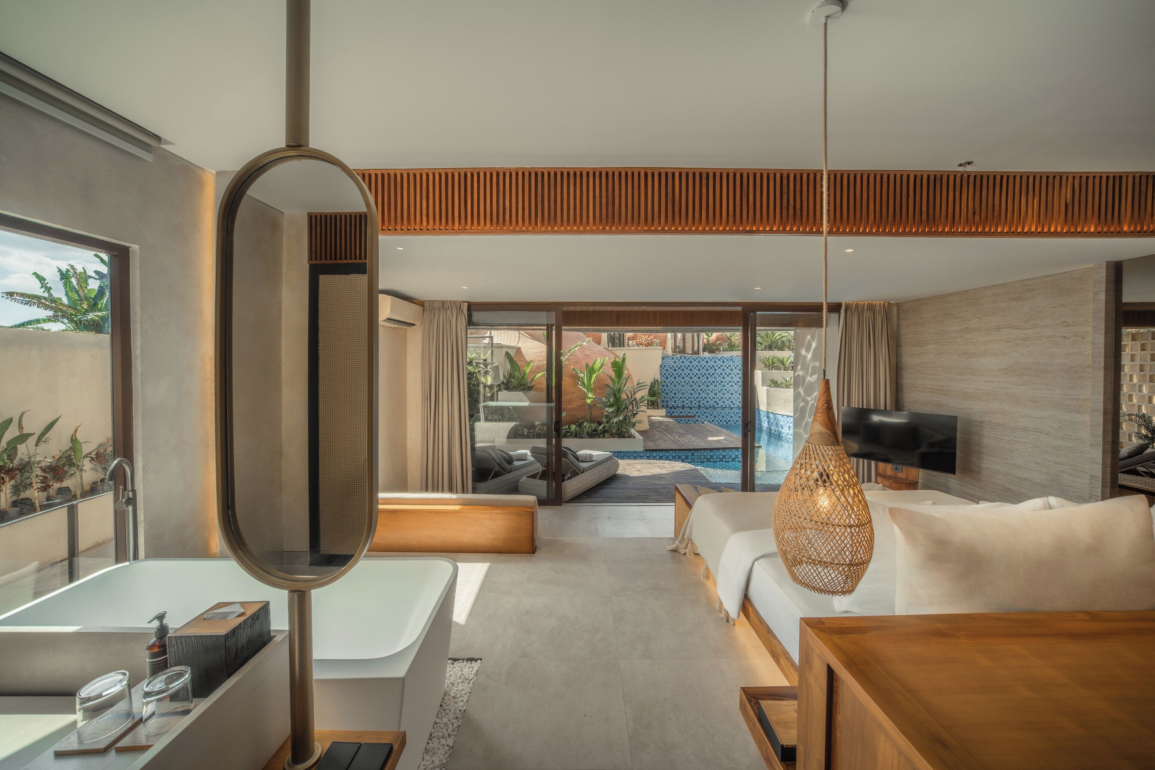 Une chambre d’hôtel moderne dotée d’une grande fenêtre, d’une baignoire, d’un canapé, d’une télévision et d’un petit espace piscine visible à travers les portes vitrées.