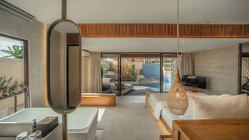 Une chambre d’hôtel moderne dotée d’une grande fenêtre, d’une baignoire, d’un canapé, d’une télévision et d’un petit espace piscine visible à travers les portes vitrées.