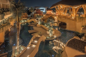 An outdoor swimming pool with a thatched roof structure, palm trees, and a night-time illuminated setting. - La Mewali Resort Canggu by Ini Vie Hospitality (Canggu)