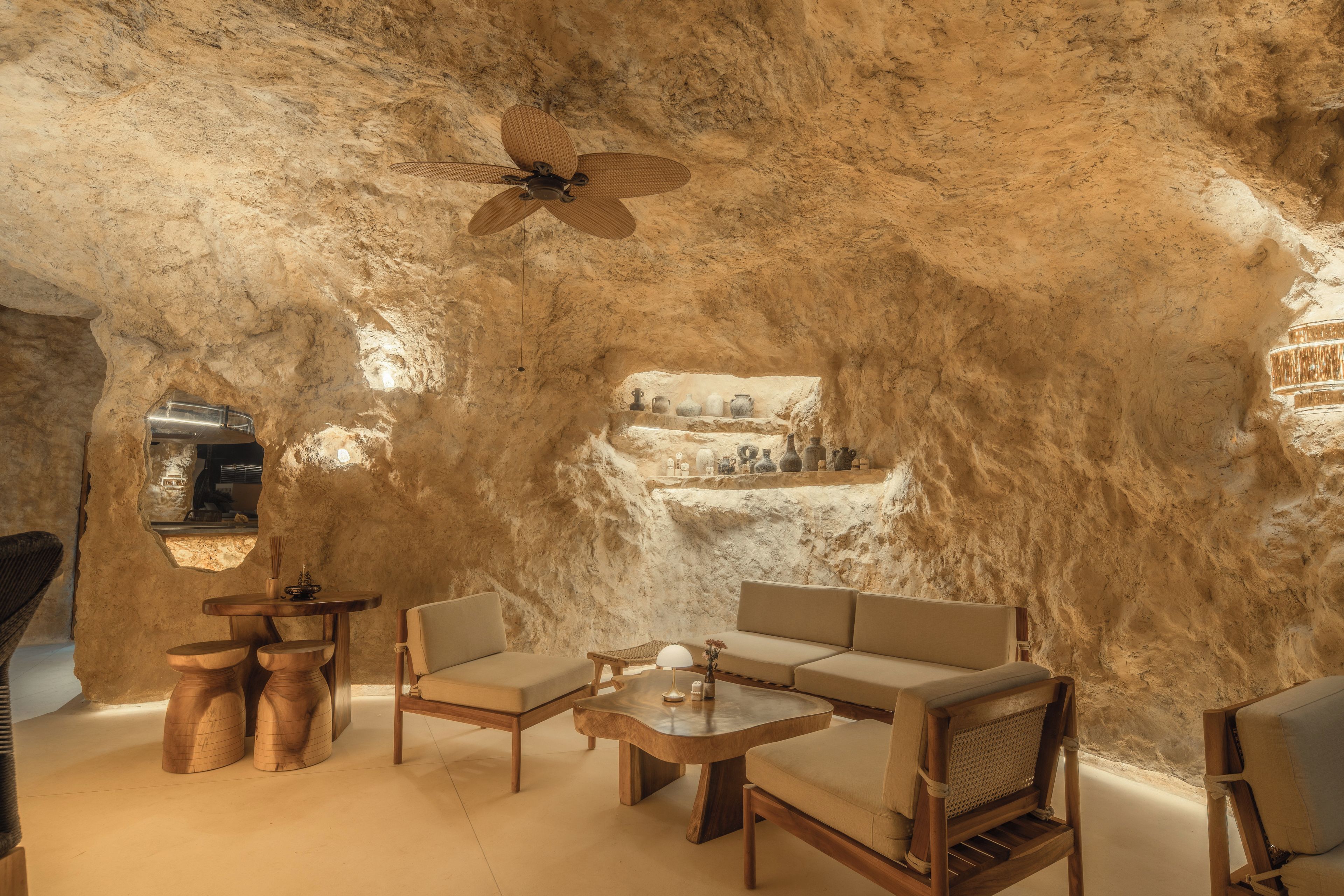 Una stanza con interni che ricordano una grotta, arredata con un divano, poltrone, un tavolo e una ventola a soffitto.