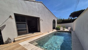Una piscina con cubierta de madera, puerta corredera de vidrio y un pequeño espacio exterior con dos sillas.