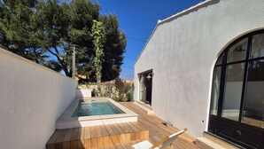 Un área de piscina exterior moderna con cubierta de madera, dos sillas de descanso y una vista despejada del paisaje circundante.