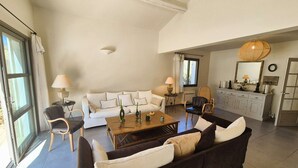 Amplia sala de estar con sofá, mesa de centro, mesa de comedor y zona de cocina con un armario y un espejo.