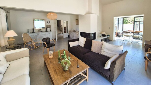Un espacio habitable amplio con un sofá oscuro, sillones blancos, una mesa de centro de madera y un ventilador de techo.