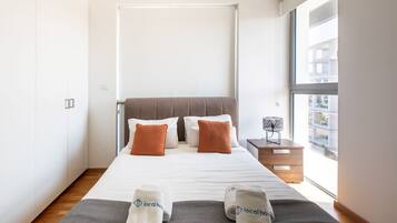 Habitación de hotel con una cama grande, una ventana con vistas a edificios, una mesita de noche con lámpara y toallas con la marca 'local host'.