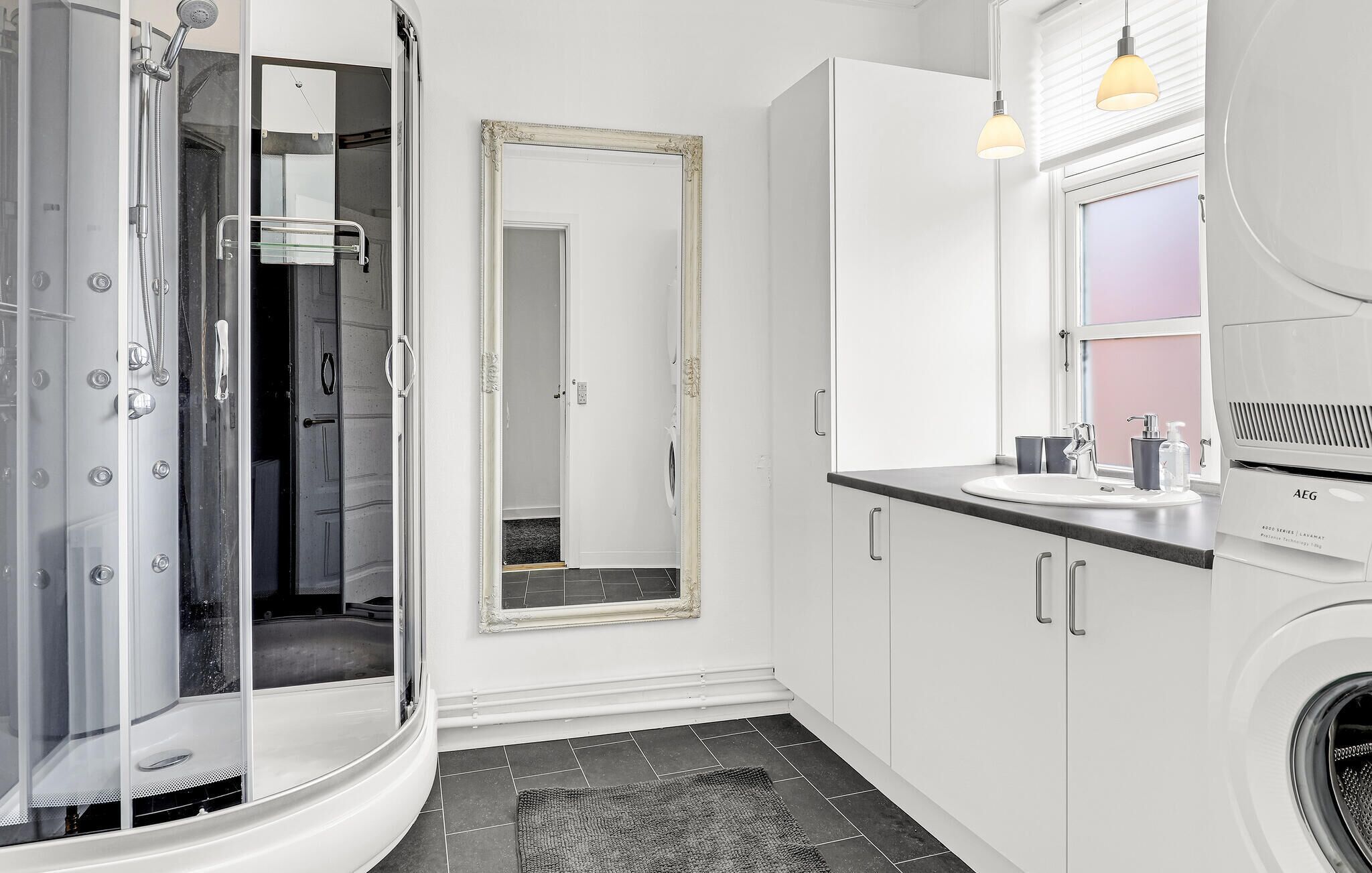 A modern bathroom with a glass-enclosed shower, a large mirror, a sink with a vanity, and a washing machine.
