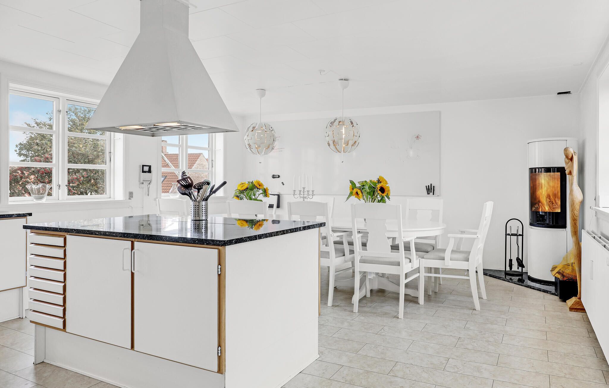 A modern kitchen with white cabinetry, a central island, and a dining area with white chairs.
