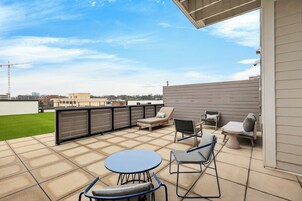 A rooftop patio with a table and chairs, a cushioned seating area, and a view of the city skyline.