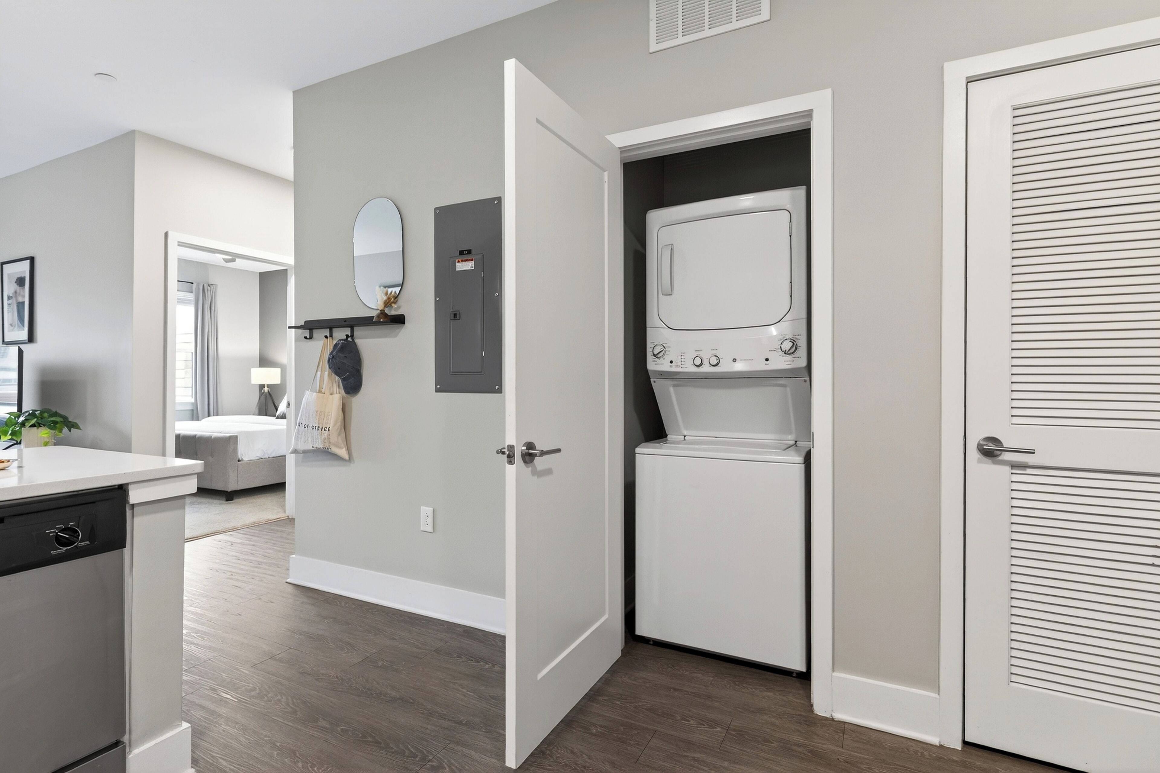 A modern laundry room with a washer and dryer, a mirror, and a door leading to another room.