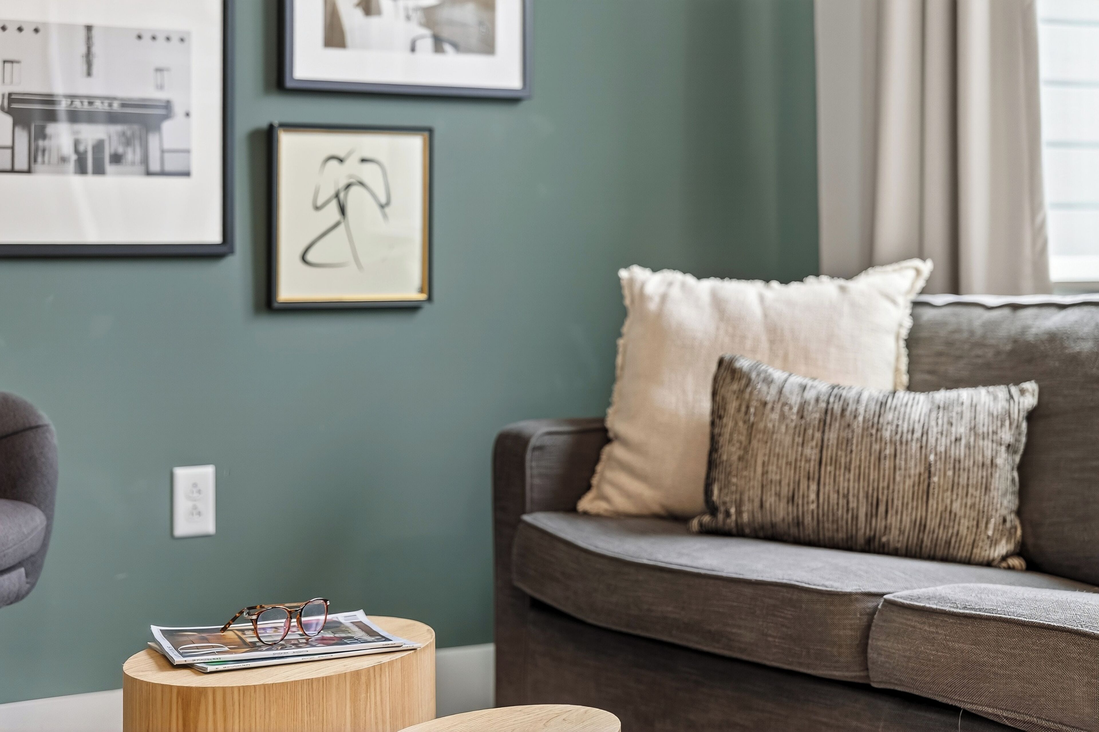 Una sala de estar con un sofá gris, una mesita redonda de madera y cuadros enmarcados en la pared.