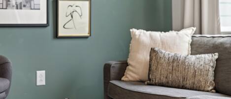 Una sala de estar con un sofá gris, una mesita redonda de madera y cuadros enmarcados en la pared.