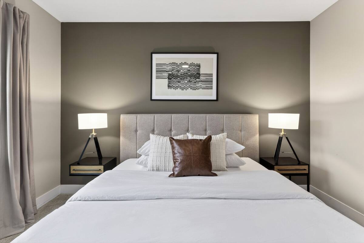 A neatly made bed with white linens, two bedside tables with lamps, a headboard, and a framed artwork on the wall.