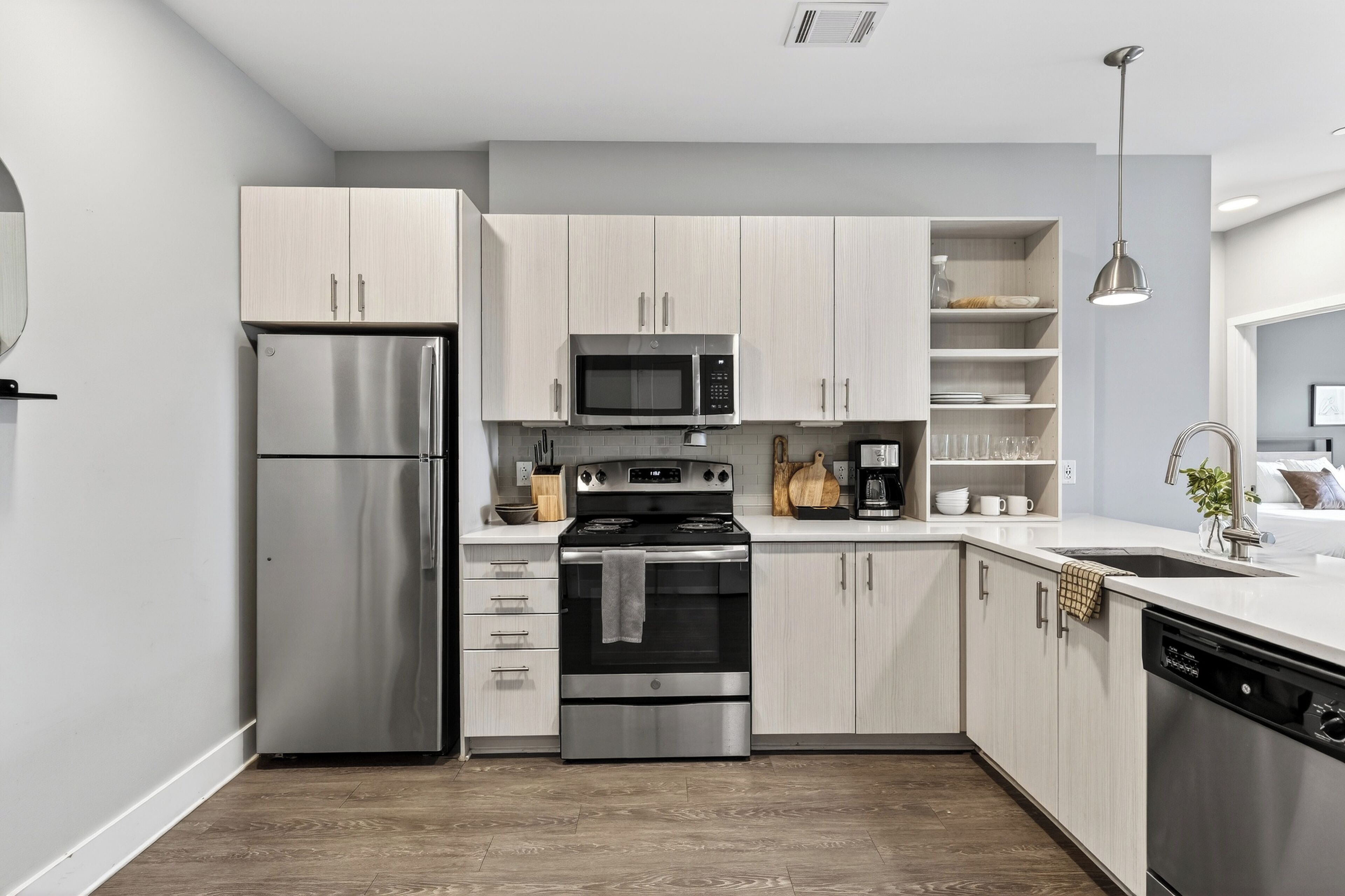 A modern kitchen with stainless steel appliances, light wood cabinets, and a white countertop.