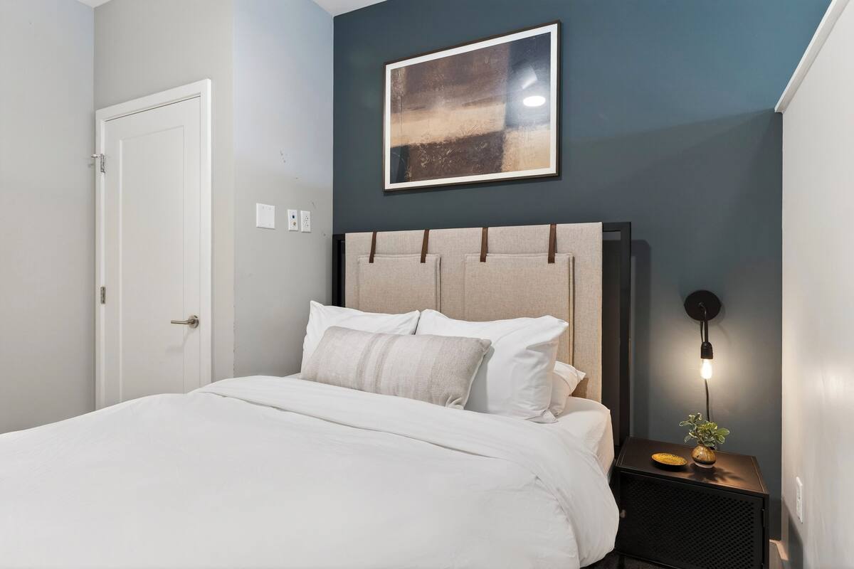 A neatly made bed with a headboard, a bedside table with a lamp, and a framed picture on the wall.