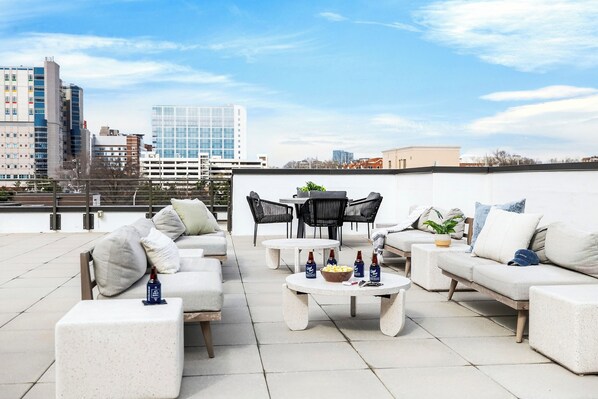 Une terrasse sur le toit avec des sièges en plein air, une table avec des collations et une vue panoramique sur la ville en arrière-plan.