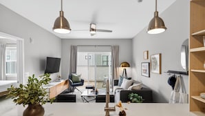 A modern kitchen with a central island, pendant lights, a ceiling fan, and a view to a living area with a sofa and coffee table.