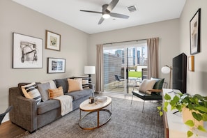 Un salon moderne avec un canapé gris, une table basse et un téléviseur. Il y a un balcon avec vue sur les immebles.