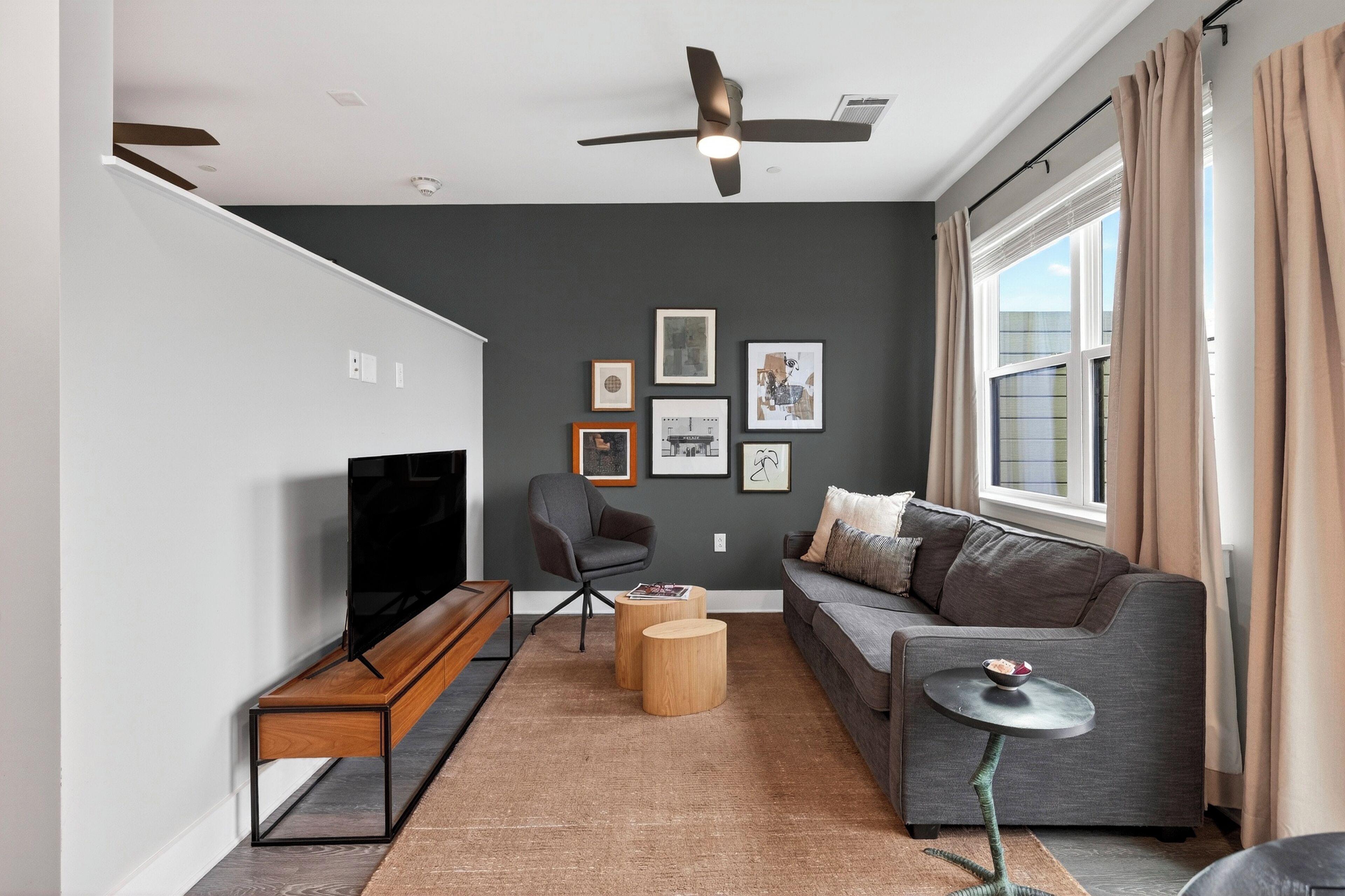 A modern living room with a sofa, a television, a ceiling fan, and framed pictures on the wall.