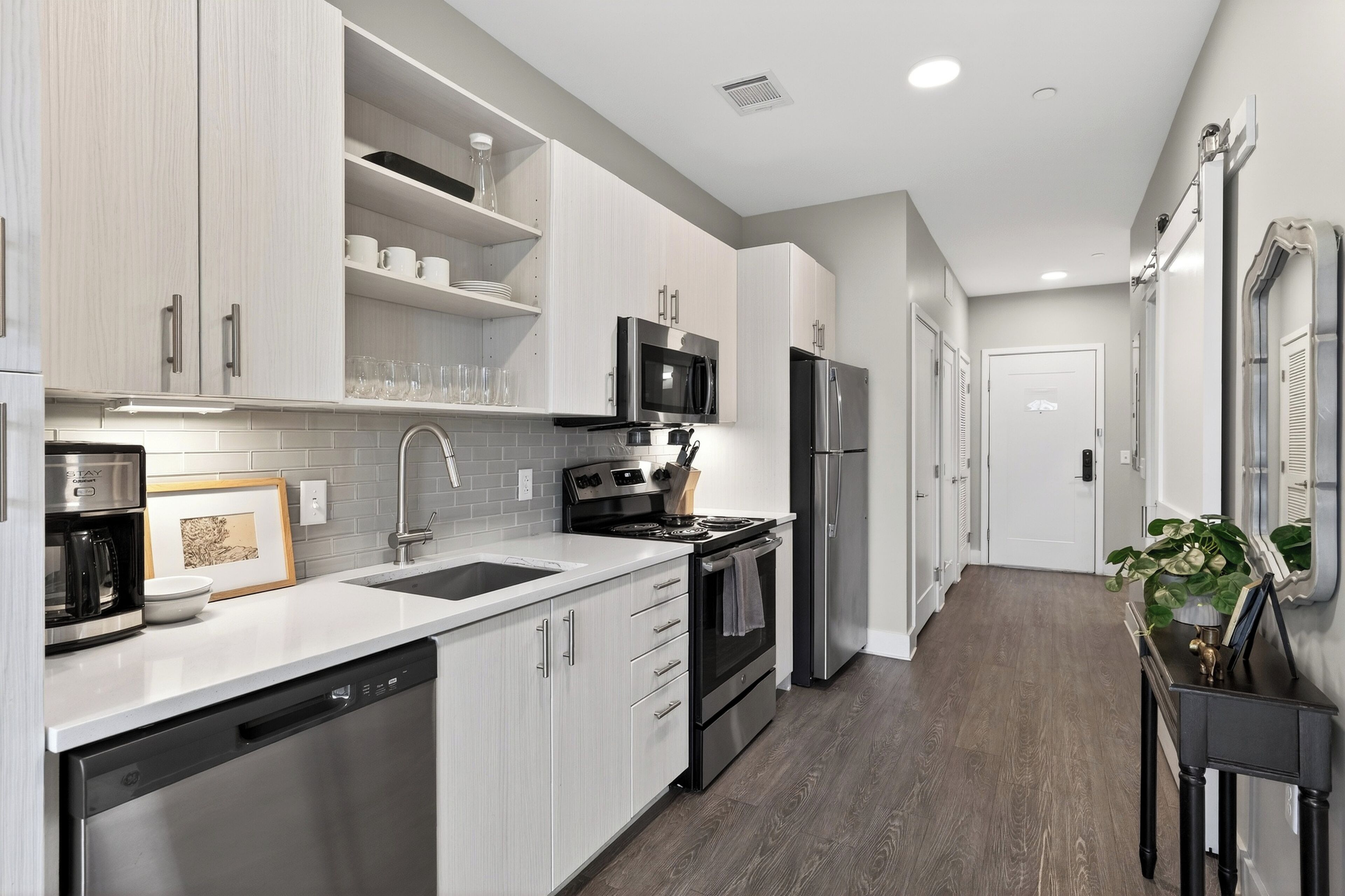 A modern kitchen with white cabinetry, stainless steel appliances, a dishwasher, and a countertop with a coffee maker.