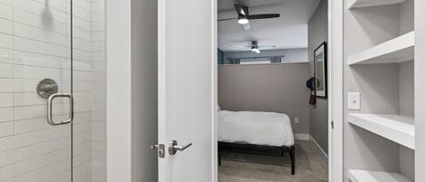 A walk-in closet with a bed, a ceiling fan, and a shower with white tiles.