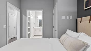 Un dormitorio con cama, mesita de noche, cabecero y puerta que da a un baño.