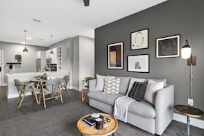 Un salon moderne avec un canapé gris, une table basse ronde et un coin repas comprenant une table et des chaises blanches.