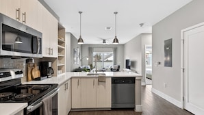 A modern kitchen with a stove, microwave, and dishwasher, wooden cabinets, and pendant lighting.