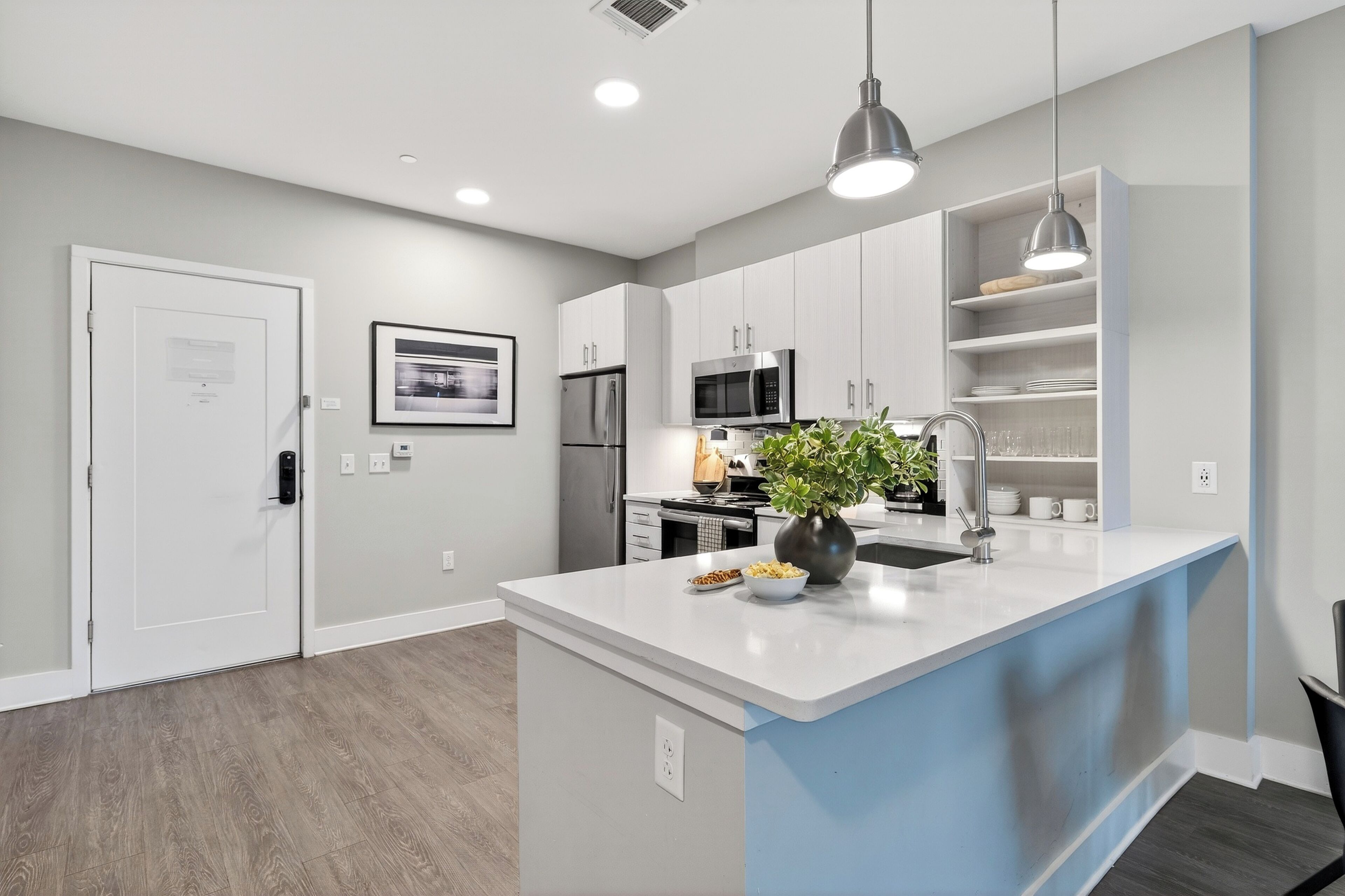 A modern kitchen with white cabinets, a central island, stainless steel appliances, and pendant lighting.