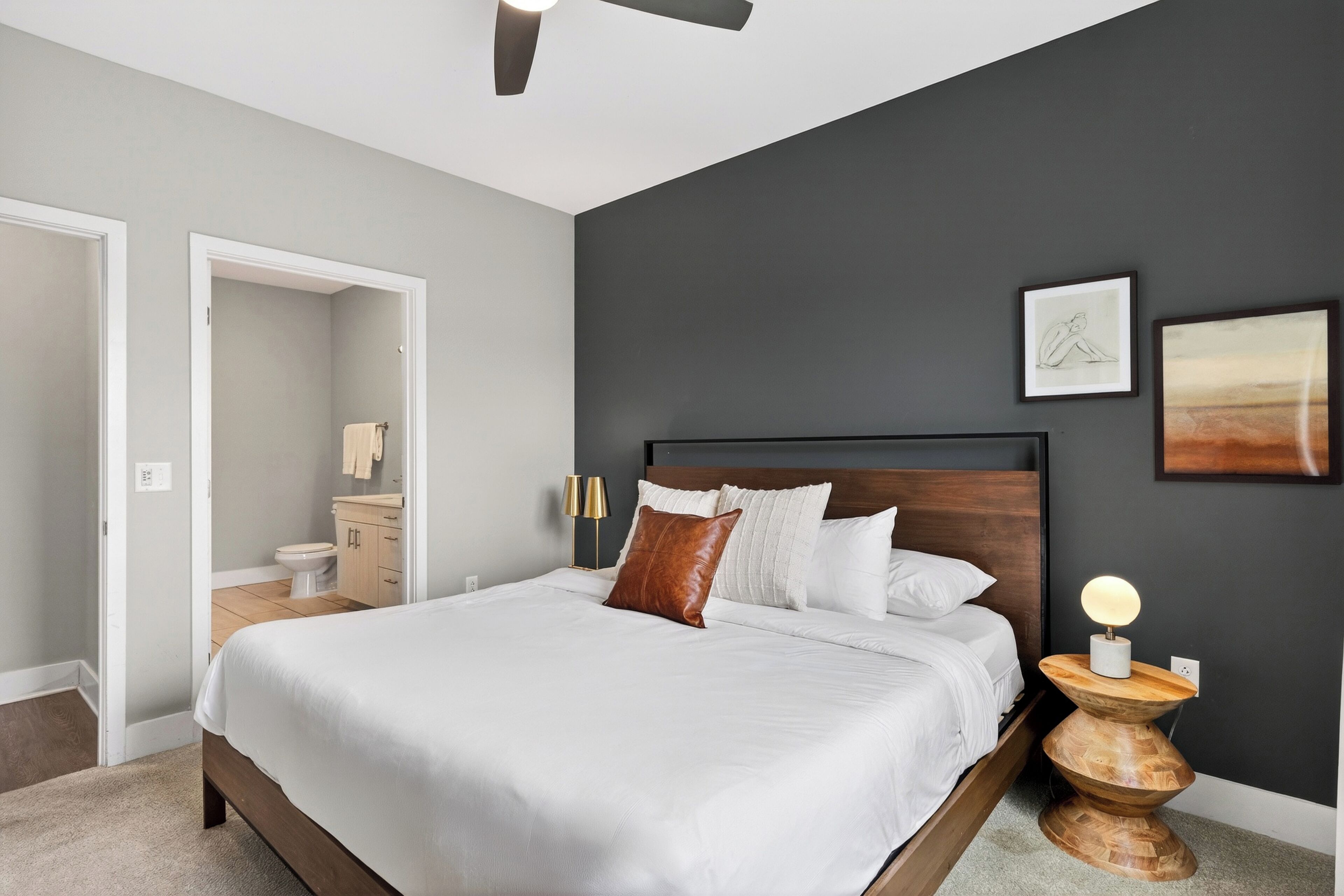 Une chambre à coucher comprenant un lit, une table de chevet, des œuvres d’art murales et un ventilateur de plafond.
