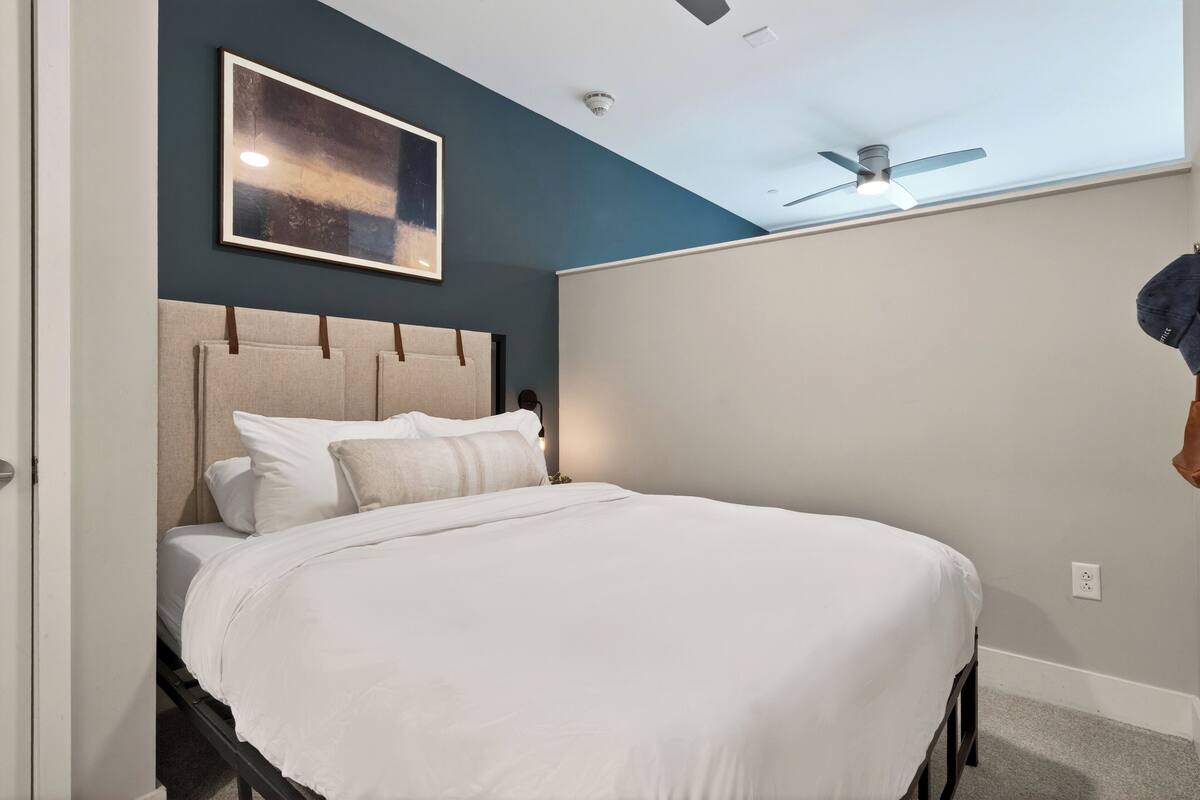 A neatly made bed with white bedding, a ceiling fan, and a framed picture on the wall.