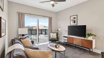 Ein modernes Wohnzimmer mit Sofa, Couchtisch, Fernseher und einem Balkon mit Blick auf die Stadt.