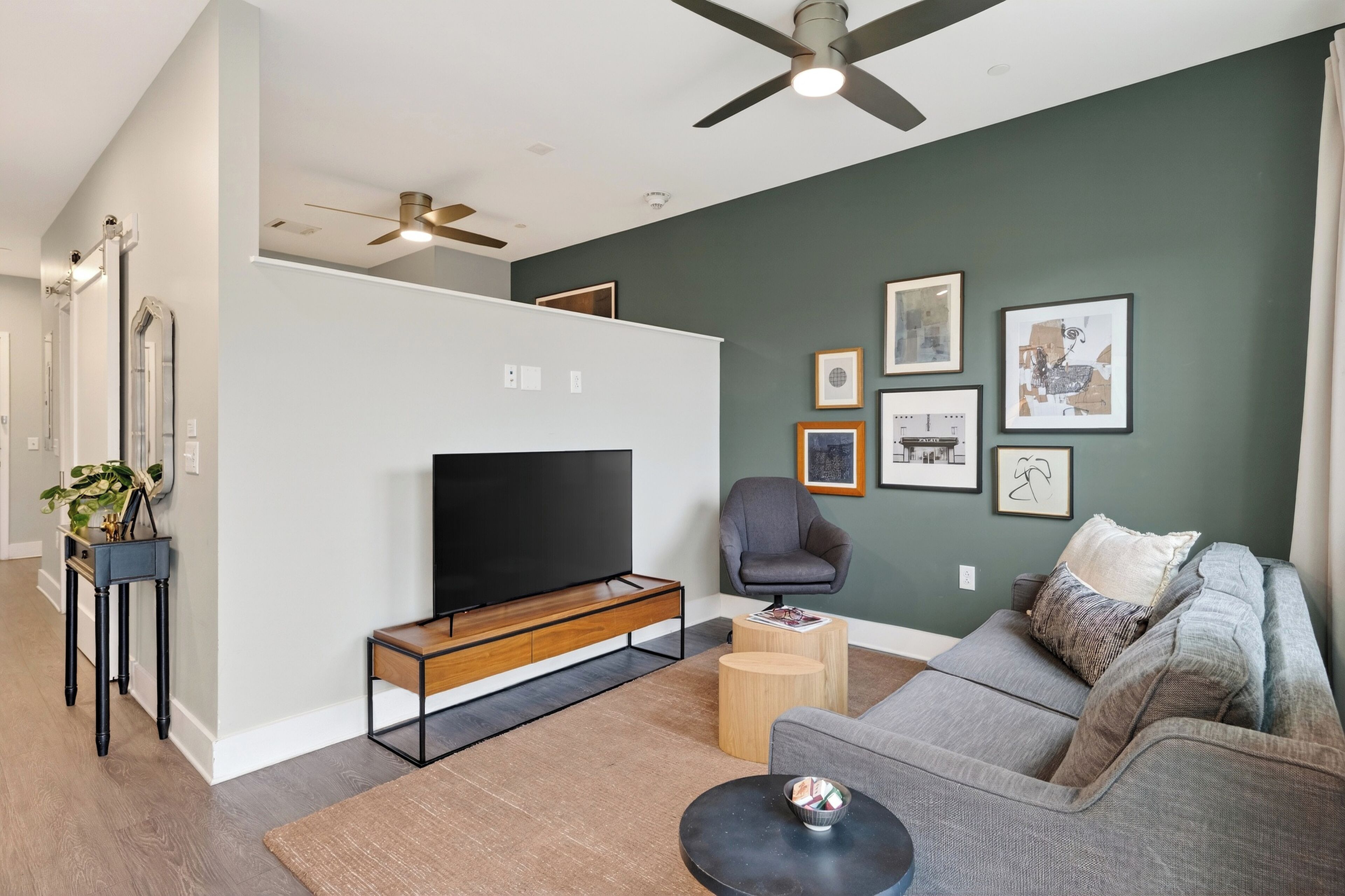 A modern living room with a flat-screen TV, a gray sofa, a wooden coffee table, and a ceiling fan.