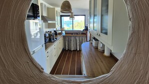 Une cuisine avec vue à travers une fenêtre circulaire, un plancher en bois et un luminaire suspendu.