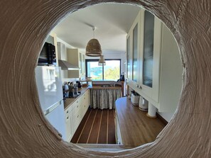 Eine Küche mit Blick durch ein rundes Fenster, Holzboden und einer Pendelleuchte.