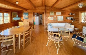A wooden cabin interior with a dining area, a living room with a sofa and chairs, and a kitchen visible through an open door. - Gorgeous home in Væggerløse with WiFi (Væggerløse)