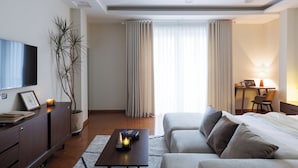 A modern hotel room with a flat-screen TV, a sofa, a desk with a lamp, and a potted plant. - Beloved Summer - 4BR Cozy & Peaceful with Elevator (Hà Nội)