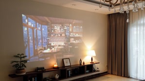 A living room with a large screen displaying a projection, a fireplace, a potted plant, a lamp, and a bookshelf. - Beloved Summer - 4BR Cozy & Peaceful with Elevator (Hà Nội)