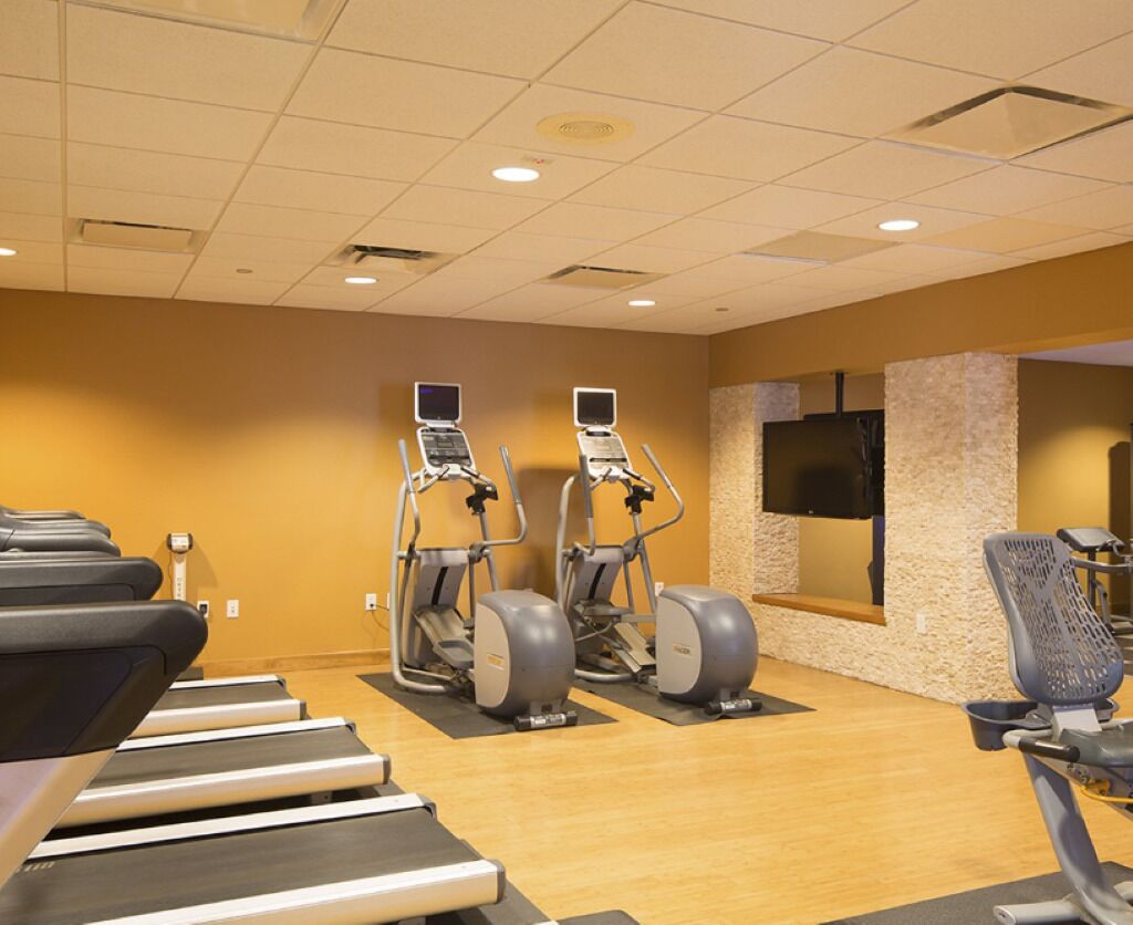 A gym with treadmills, elliptical machines, and a TV mounted on the wall.