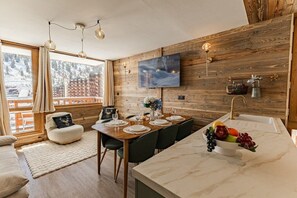 Eine moderne Küche mit Holzwand, einem Essbereich mit Tisch für vier Personen und einer Obstschale auf der Arbeitsfläche.