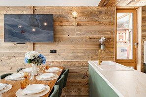 Ein Holzinterieur mit einem für vier Personen gedeckten Esstisch, einem wandmontierten Fernseher und einer Küchenzeile mit Spüle.