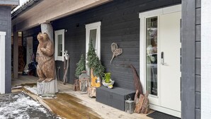 Ein Holzhaus mit Veranda, einer Bärenskulptur, einem Weihnachtsbaum und einer Tür mit Fensterteil.